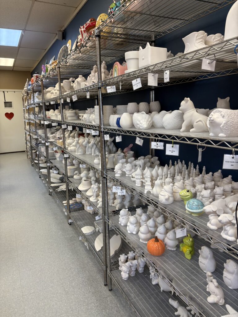 A large selection of paint your own pottery pieces are displayed on shelves.