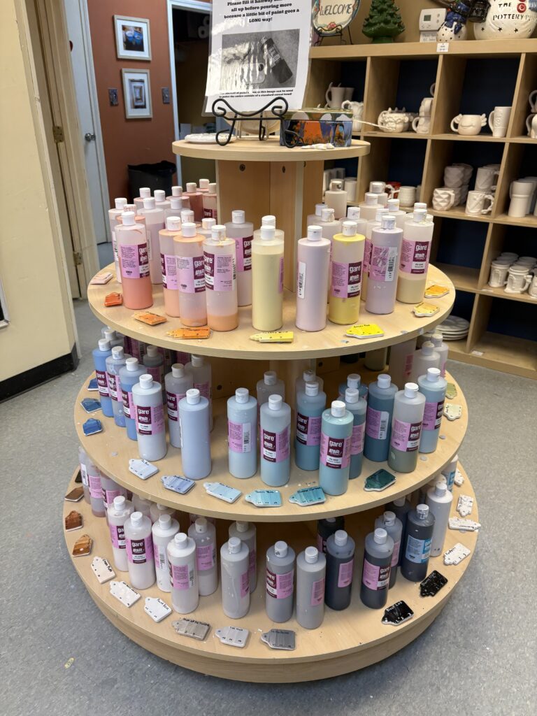 The paint for paint your own pottery is shown on a display. The colors go from warm to cool.