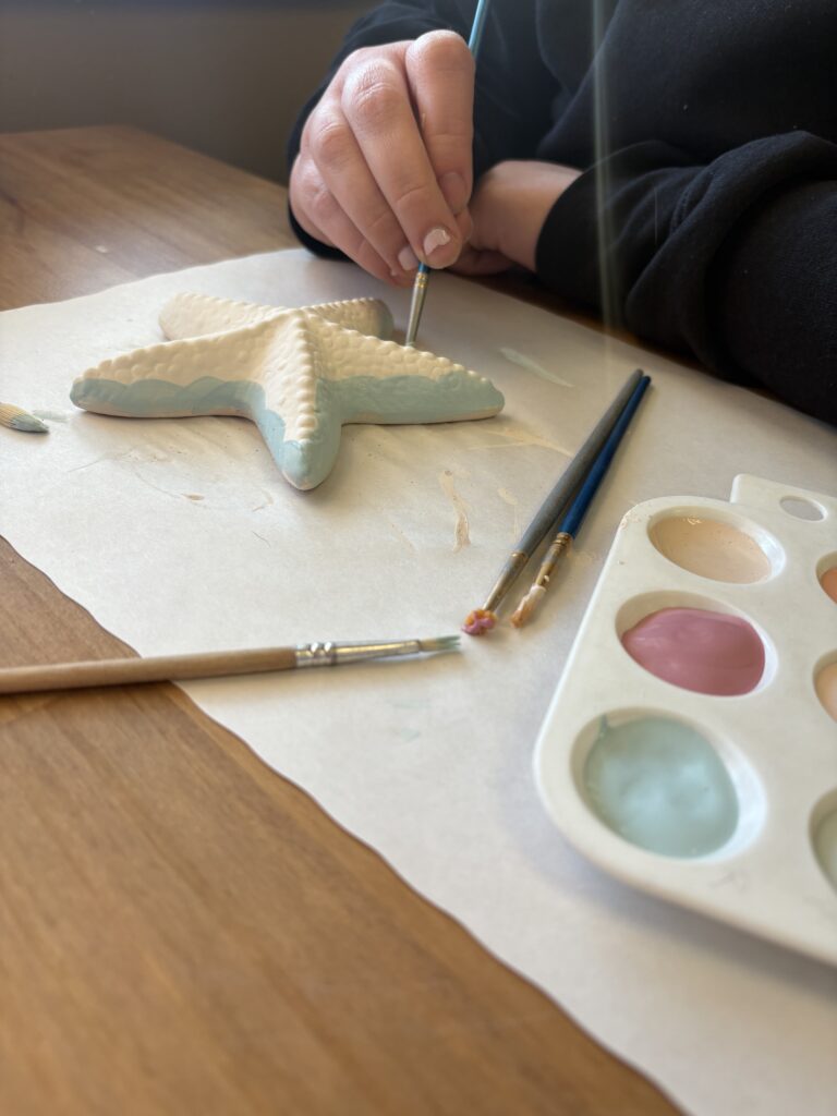 The starfish piece is on the table and being painted with light blue paint in wavy lines