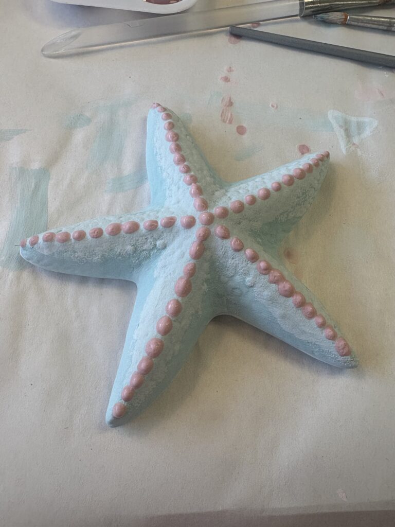 A light blue starfish paint your own pottery piece is shown with pink dots on top