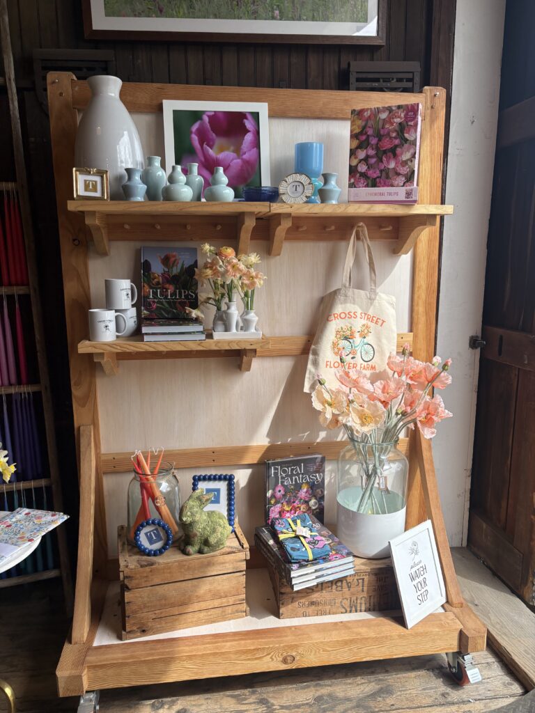 A display is shown with fake, pink flowers, various blue vases, white and blue mugs, a blue candle, and a floral book