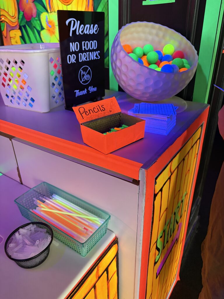 A desk offers brightly colored golf balls, glow bracelets, pencils and scorecards upon entering