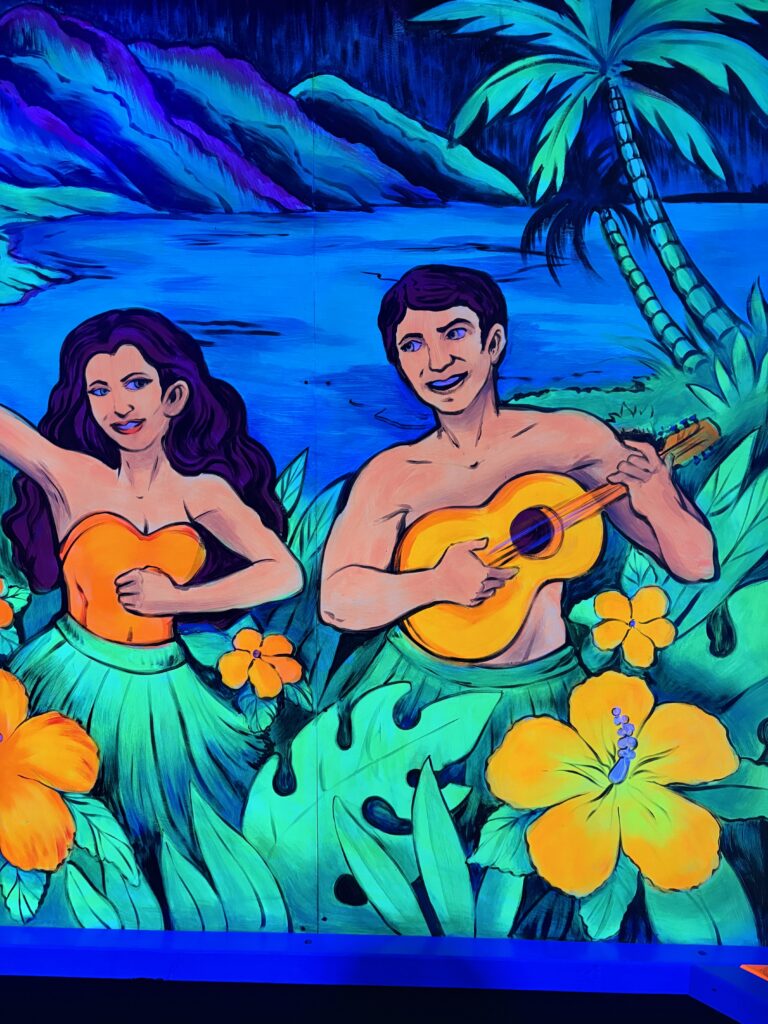 A mural of a woman dancing while looking at a man strumming the ukulele orange Hawaiian flowers surround them 
