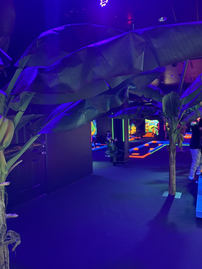 Faux banana trees in the middle of the indoor mini golf venue are shown
