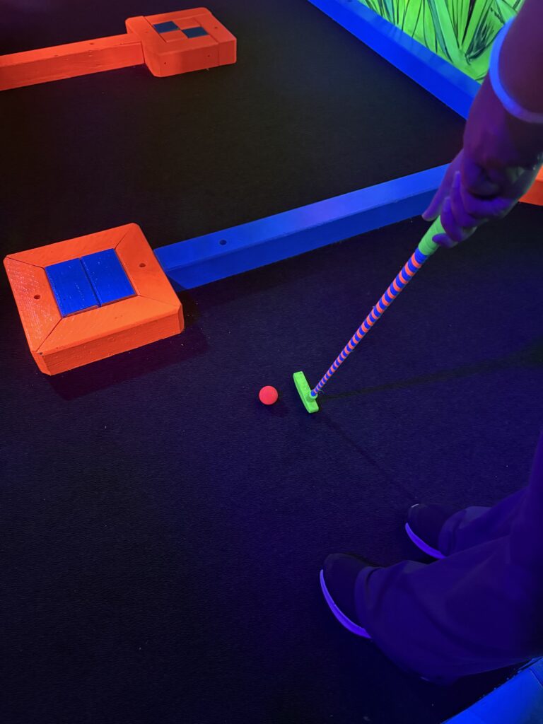 A person putting a pink ball on the mini golf course