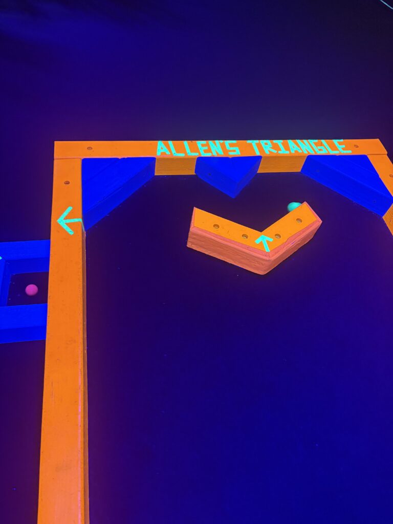 A wood course piece that says "Alien's Triangle" with a green ball going into the hole is shown