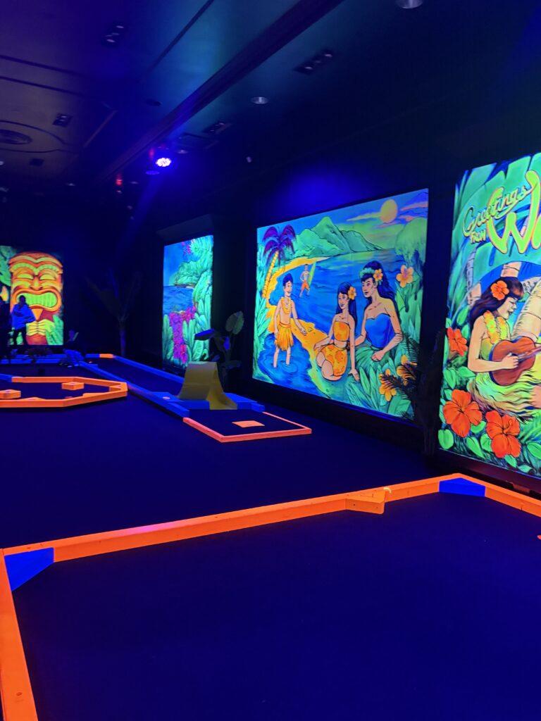 The indoor mini golf course is shown with the colorful tropical murals on the walls