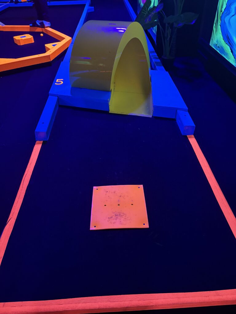 A yellow tube ramp for mini golf is shown on a course