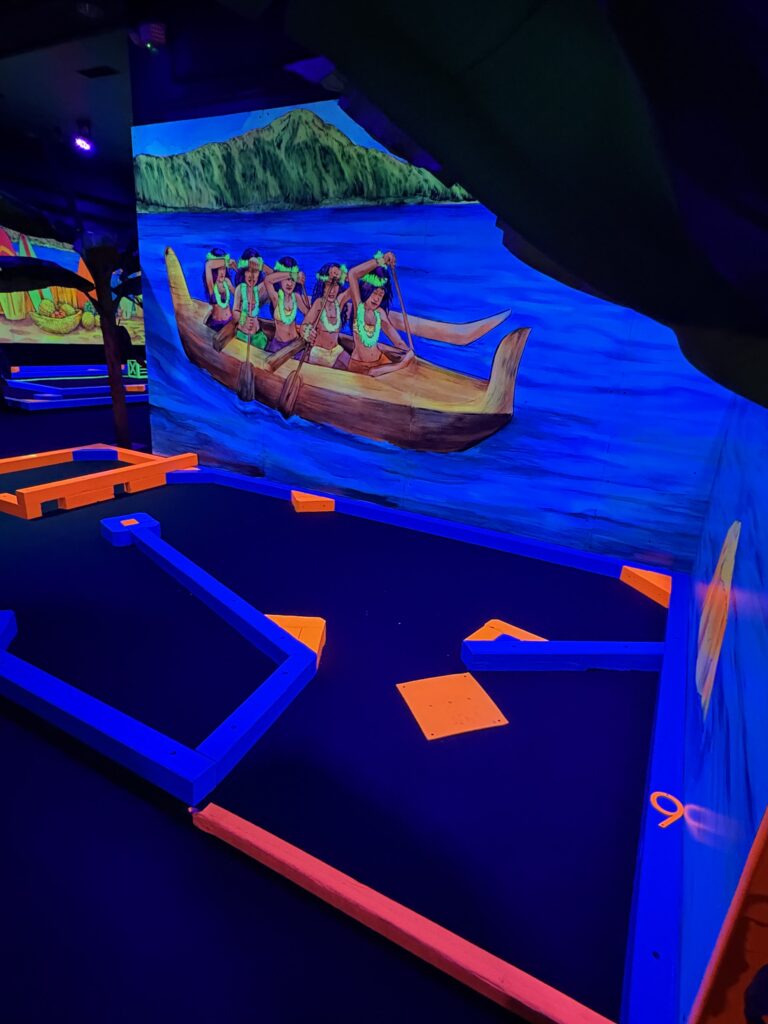 A mural of five people rowing a boast is glowing on the wall near Hole 9