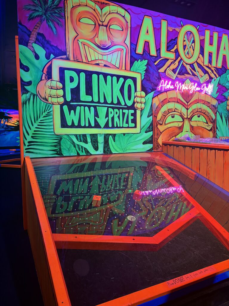 Tiki figures are painted on the wall of the last hole and a red frame with a Plinko board is shown