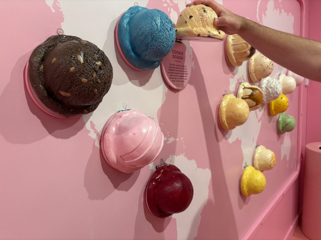 Hyperrealistic plastic scoops of ice cream on a map of the world. A man's hand is lifting a scoop revealing a fact underneath.